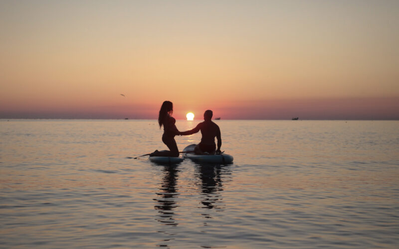 Coppia sulla spiaggia all’alba, illuminata da una luce morbida e naturale.