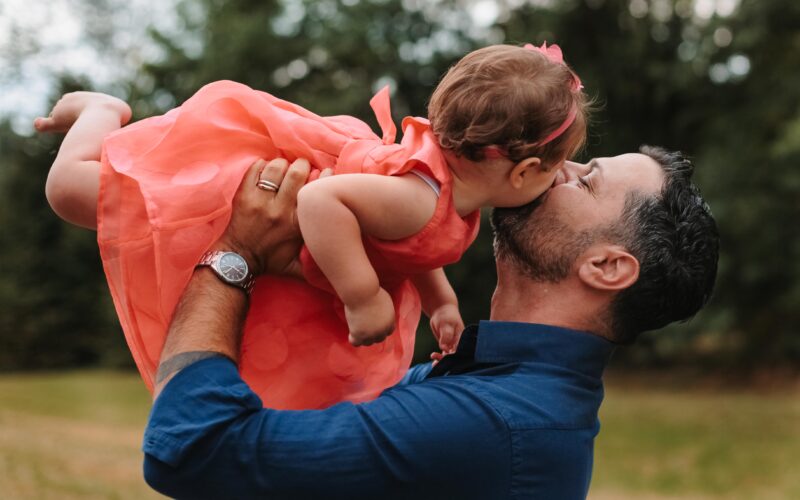 Papà che gioca con la sua bimba al parco in una giornata estiva, in un momento spontaneo e pieno di dolcezza.